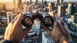 © sungedi - Hands holding binoculars view a cityscape at sunset