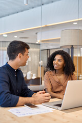 Aufkleber - Two young diverse coworkers business people using laptop and talking at office meeting. Busy happy team professional employees working together on computer discussing online technology data at work.