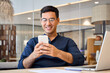 © insta_photos - Smiling busy professional Hispanic business man sitting in office holding mobile cellphone. Young happy businessman entrepreneur using smartphone looking at cell phone technology device at work.