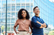 © insta_photos - Young happy smiling professional office team of two diverse confident female and male partners business people man and woman standing outdoors on city street looking at camera, corporate portrait.