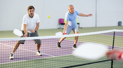 Wall Mural - Athletic men playing pickleball tennis on the pickleball court indoors