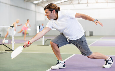 Wall Mural - Athletic man and his partner playing pickleball tennis on the pickleball court indoors