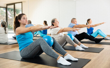 Wall Mural - Class of people of different ages holding balls between legs and pushing press during Pilates training in studio