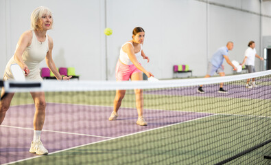 Two athletic women of different ages are playing a game of pickleball on a court inside a sports facility