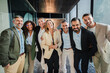 © Jose Calsina - Diverse group of smiling business professionals standing together in office corridor, dressed in formal attire, celebrating teamwork, success, corporate unity and collaboration while posing happily