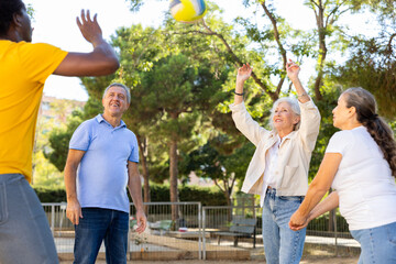 Social club of joyful older diverse people enjoying volleyball on the October sunny day outdoors