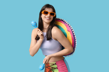 Young woman with colorful sombrero and maracas on blue background. Cinco de Mayo celebration