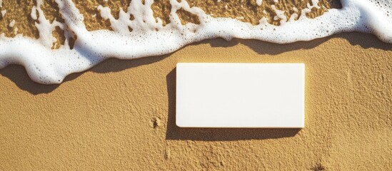 Poster - Blank white business card lying on sandy beach with ocean waves for branding or design purposes Copy Space