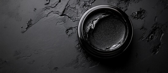  - Black circular container with dark substance on textured black background, featuring Copy Space for text placement.