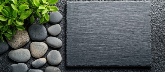 Poster - Black slate stone surface with smooth river stones and green leaves, suitable for copy space and natural decor themes.