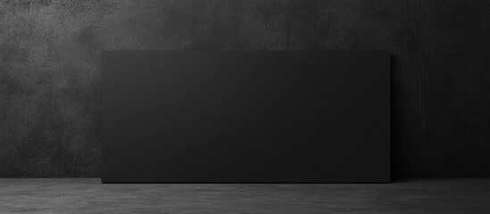Poster - Black blank rectangular panel against a dark textured wall in an indoor setting with ample copy space for text insertion