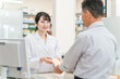 © buritora - 薬局で薬の相談を受ける高齢者男性と薬剤師・調剤師の女性