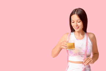 Poster - Beautiful young happy Asian woman in sportswear with measuring tape and cup of tea for weight loss on pink background