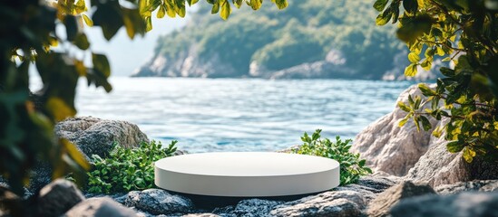 Aufkleber - White circular podium on rocky beach surrounded by lush greenery and serene blue water with natural light highlighting blank space for text.