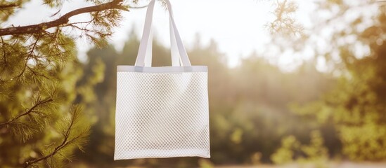 white mesh tote bag hanging from a tree branch in a natural setting with soft sunlight and blurred t