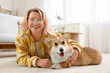 © Pixel-Shot - Beautiful happy mature woman with cute Corgi dog lying on floor in living room