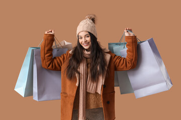 Poster - Beautiful young woman in warm clothes with shopping bags on brown background