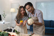 © crizzystudio - Loving couple smiling and showcasing fresh vegetables while preparing a healthy meal together in their modern kitchen, enjoying moments of joy and togetherness