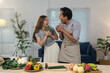 © crizzystudio - Cheerful couple is playfully using broccoli and bell peppers as microphones, enjoying their time together while preparing a healthy meal in their modern kitchen
