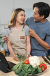 © crizzystudio - Young asian couple having fun in the kitchen preparing a healthy vegetarian meal following instructions on a digital tablet, he is feeding her with a slice of cucumber