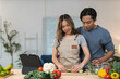© crizzystudio - Young asian couple preparing a healthy meal together in their modern kitchen, following an online recipe on a tablet, promoting healthy eating and bonding