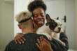 © Seventyfour - Portrait of joyful African American woman arriving home gently hugging boyfriend holding small pied French bulldog though expressing adoration and love