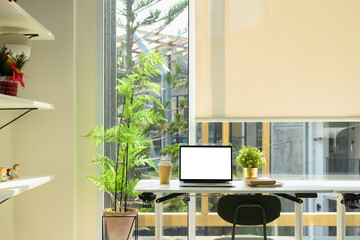 Wall Mural - Stylish workspace with blank laptop screen, potted plants, and a coffee cup