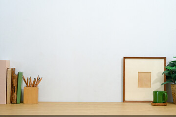 Rustic workspace with pencil holder, vintage books, a coffee mug, and picture frame against white wall