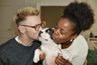 © Seventyfour - Portrait of excited Black woman and her boyfriend hugging and kissing little French bulldog sharing love and affection for little pet captured at home, camera flash