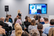 © Anton Gvozdikov - Diverse audience attentively listening to a speaker at a business conference. Presentation displayed on a big screen in a modern meeting room setting.
