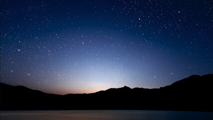 Wall Mural - a movement of stars in the night sky with the view of mountains..