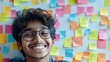 © Veronika - Smiling young boy with glasses in front of colorful sticky notes in a bright learning environment