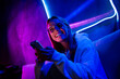 © deagreez - Photo of cute lovely blonde girl hold telephone smile nightclub sit couch purple blue neon late night blogger indoors house late