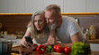 © Yuliia - Caucasian married couple bonding family old mature woman man read cooking recipe on mobile phone senior 50s husband wife talking hugging shopping online food order with smartphone together in kitchen