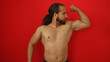 © Krakenimages.com - Young man with beard poses confidently flexing muscles against vibrant red wall