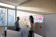 © ReeldealHD images - Coworkers discussing business strategy using adhesive notes to brainstorm in an office
