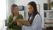 © Krakenimages.com - Women working together in an office, one older and one younger, looking at clipboard and discussing work intently.
