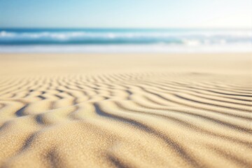 Poster - Abstract ripples on sandy beach with blurred ocean and blue sky background.