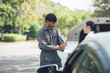 © Kritdanai - Roadside Assistance: A professional roadside mechanic consults with a customer, reviewing paperwork at the scene of a vehicle breakdown.  The image conveys a sense of trust and reliability.