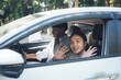 © Kritdanai - Road Trip Adventures: Two diverse young women, one Black and one Asian, cheerfully wave from inside a car, embarking on a spontaneous road trip.  The image exudes energy, excitement.
