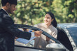 © Kritdanai - New Car Excitement: A young woman beams with excitement as a salesperson hands her the keys to her brand new car, captured in a moment of pure joy and anticipation.