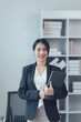 © Kritdanai - Confident Businesswoman: A portrait of a smiling, young businesswoman holding a laptop, exuding confidence and professionalism in her modern office setting. 