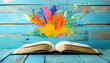 © imran - Open book with a splash of colorful paint above, set against a turquoise wooden background, blending creativity and literature  -