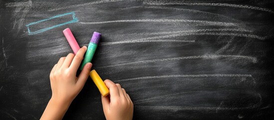 Aufkleber - Hands holding colorful chalk markers on a blackboard with ample empty space for text or creative ideas in an educational setting.