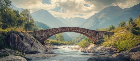 Aufkleber - Scenic stone bridge spanning tranquil river in rocky valley surrounded by lush greenery and majestic mountains under a dramatic sky