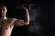 © New Africa - Man with talcum powder on hand training with barbell against black background. Space for text