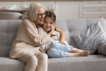 Wall Mural - My little beloved grandchild. Affectionate loving old age grandmother hug embrace with love warmth tenderness care small preteen age girl grandkid talk with child spend time together on couch at home