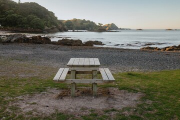 Wall Mural - Empty picnic table on a pebble beach at sunrise. Coastal scenery. Perfect for a relaxing break. Matauri Bay, Matauri Bay, Northland, NZ