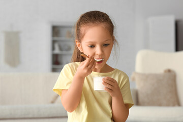 Wall Mural - Cute little girl with spoon eating yogurt at home