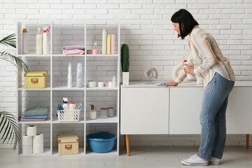 Canvas Print - Young woman with rag and detergent cleaning white cabinet at home